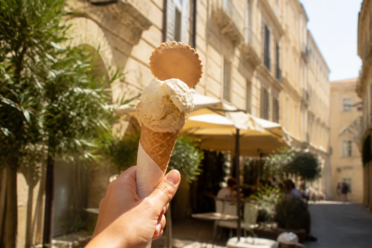 Cornet de glace tenu à la main devant une façade ensoleillée de Montpellier